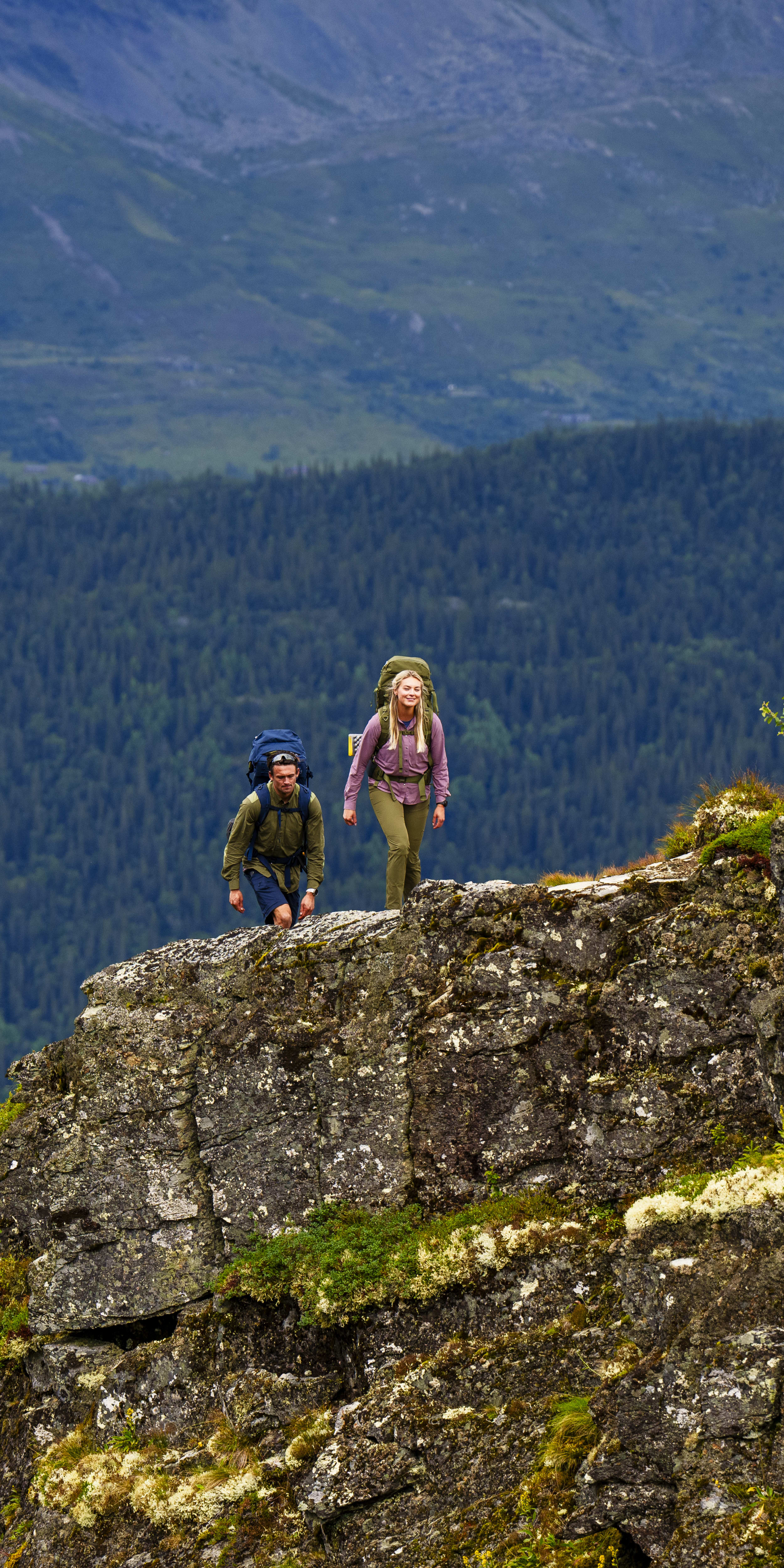 Two people in Norrøna gear hiking on a rocky mountainside. The background is a mountain range.
