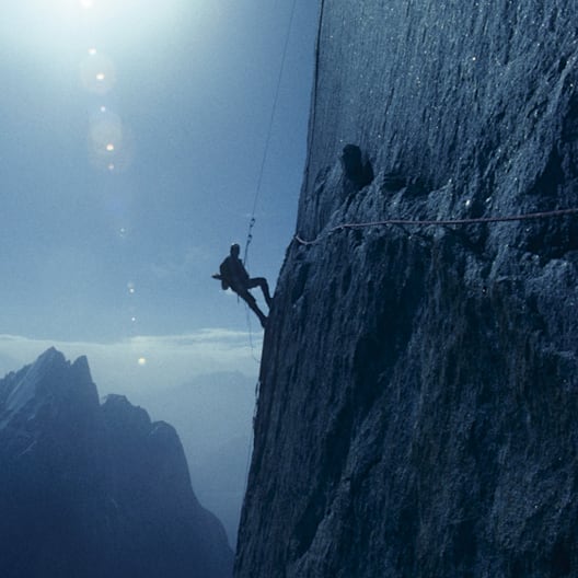 Silhouette of a climber rappelling down a steep rock face with a mountain range in the background. 
