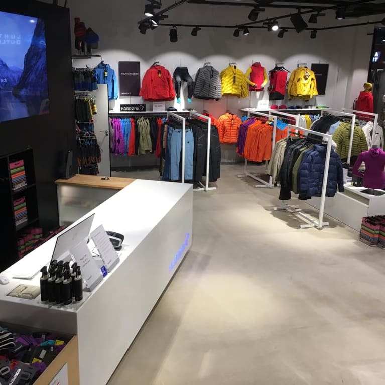 Norrøna retail store interior showing colorful outdoor clothing on display racks and a sleek white sales counter.