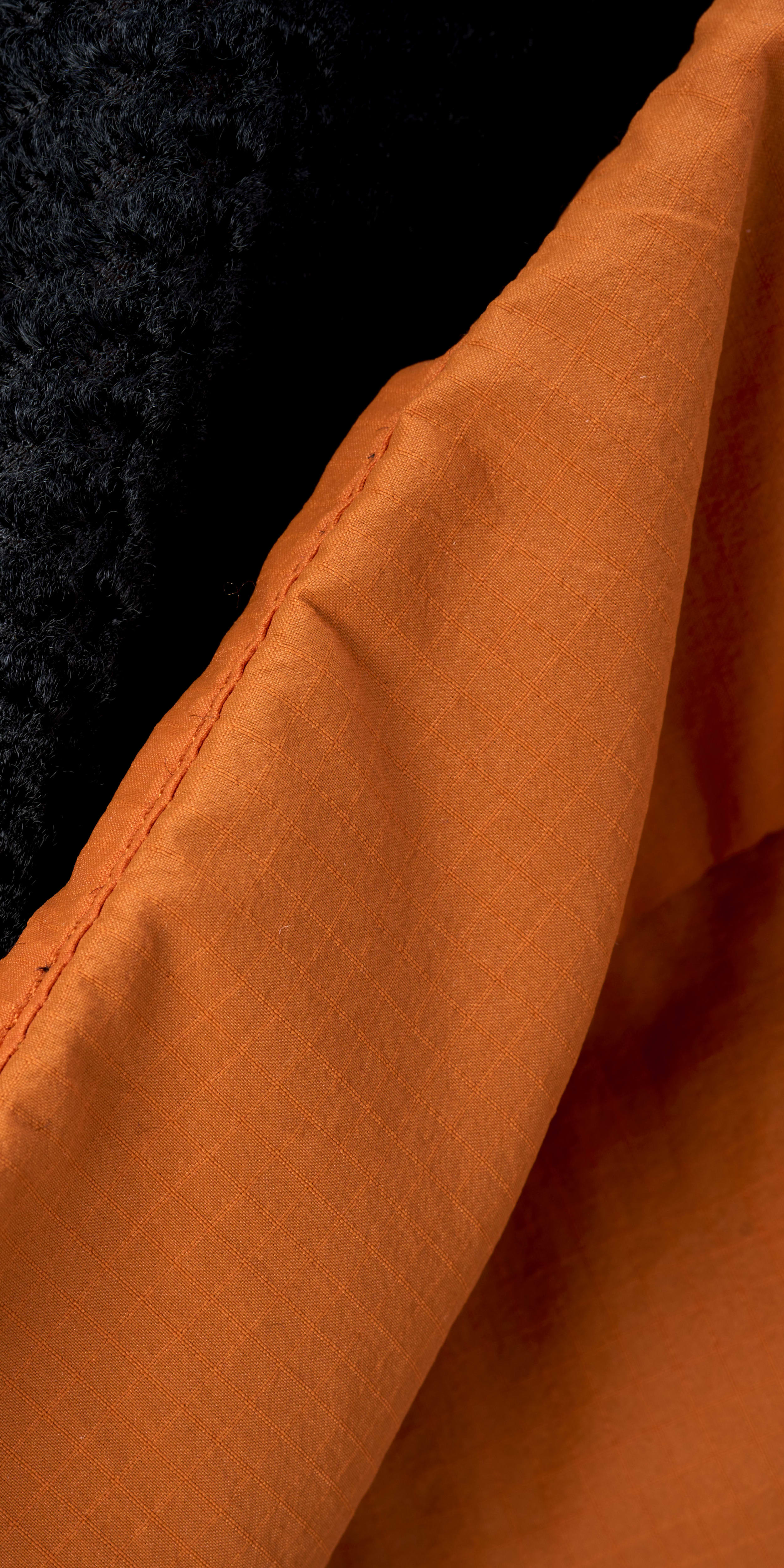 Close-up of an orange Norrøna jacket with a black fleece lining.  
