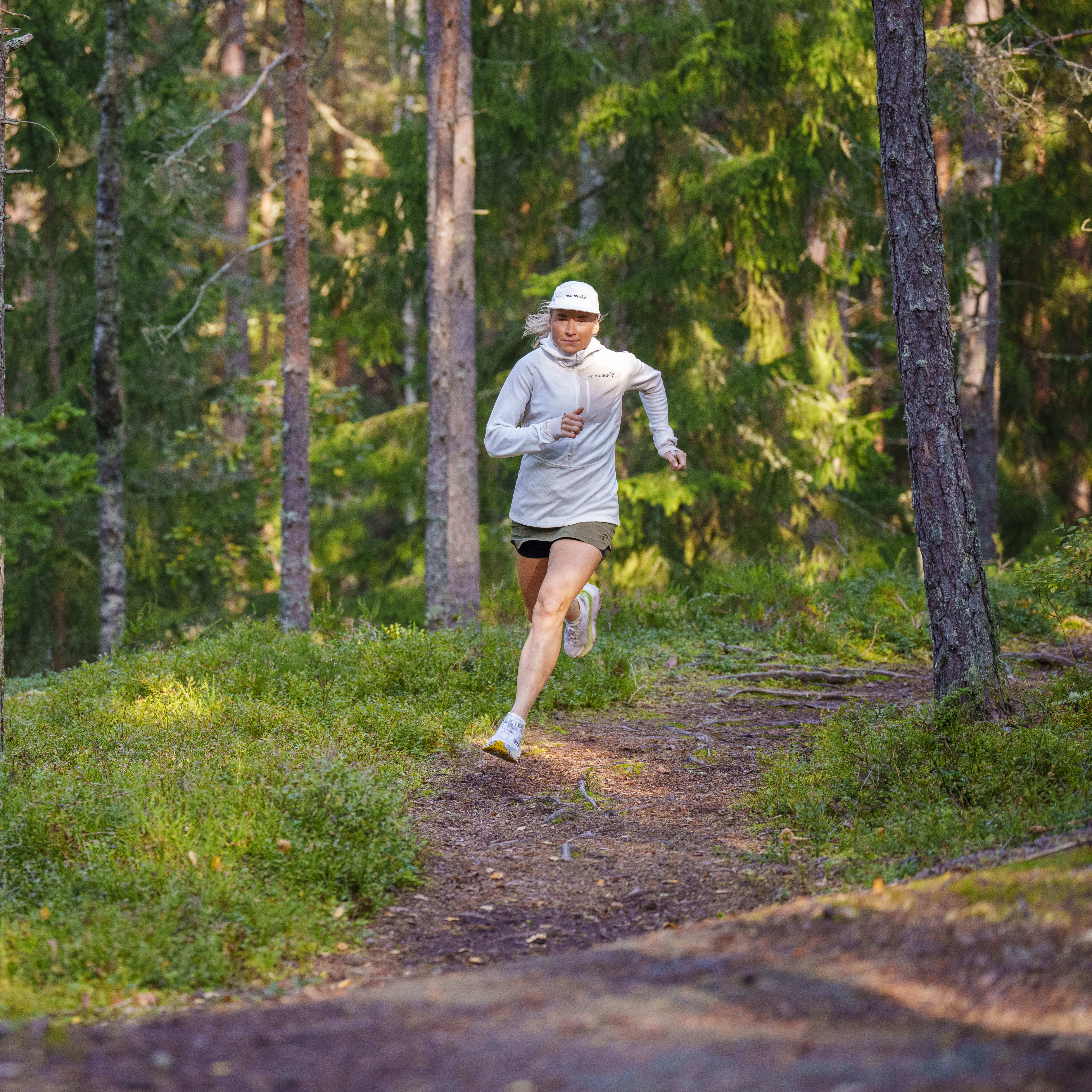 A person wearing a Norrøna jacket runs on a forest trail. 
