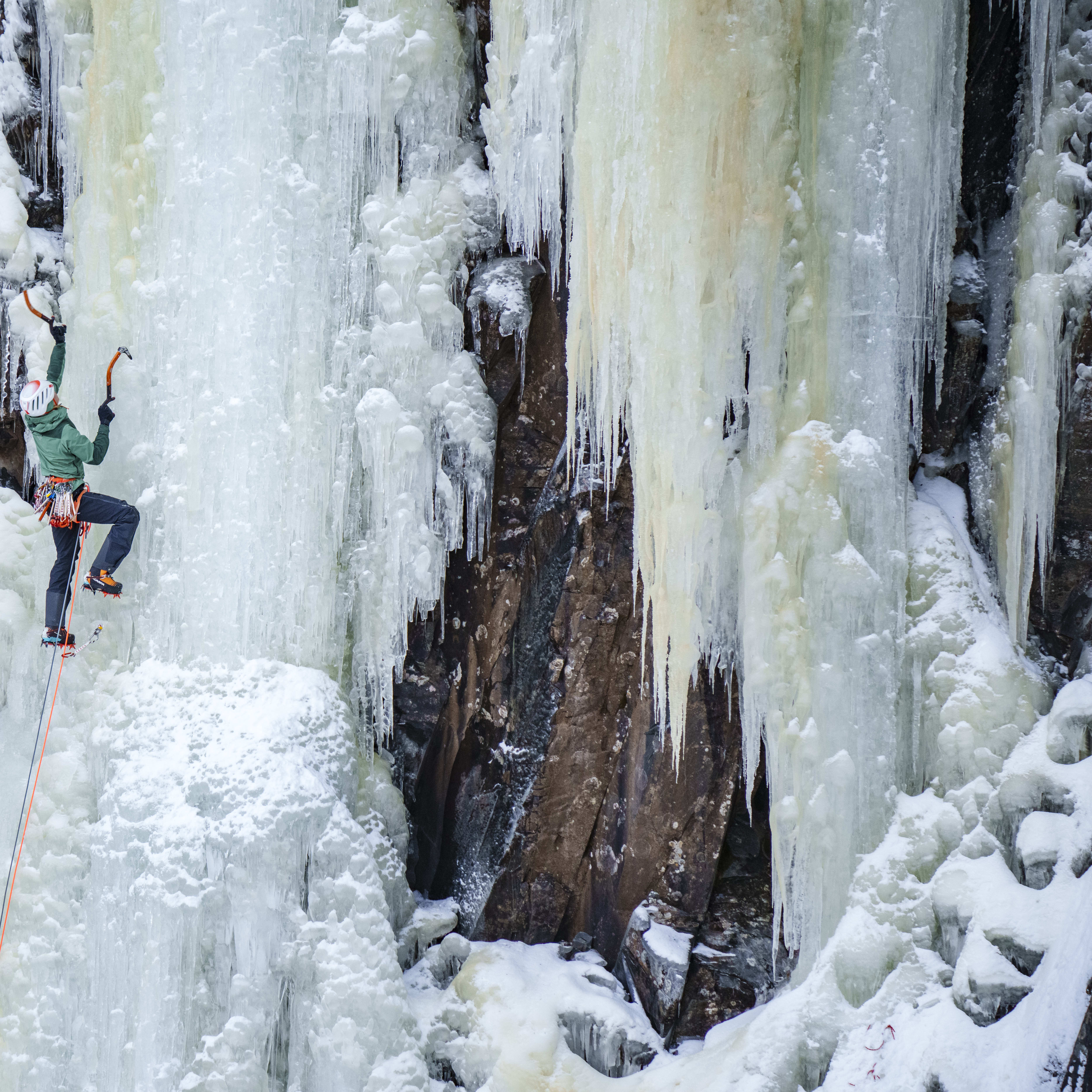 A person ice climbing a frozen waterfall wearing a Norrøna jacket and helmet. 
