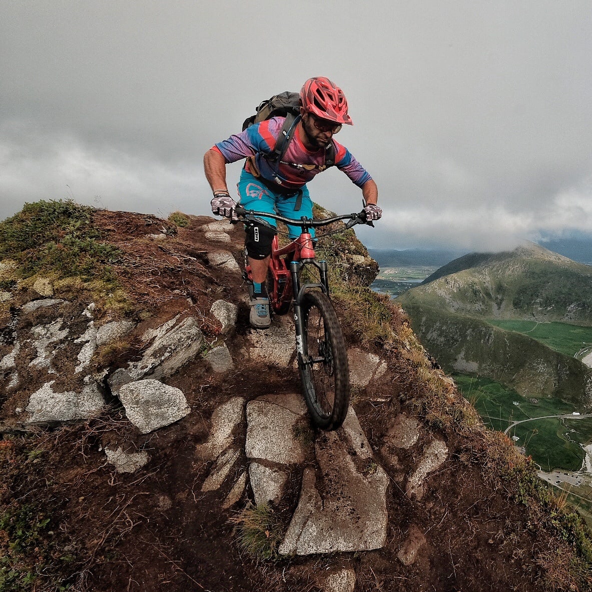 A man riding a mountain bike on a rocky trail overlooking a turquoise ocean bay. 
