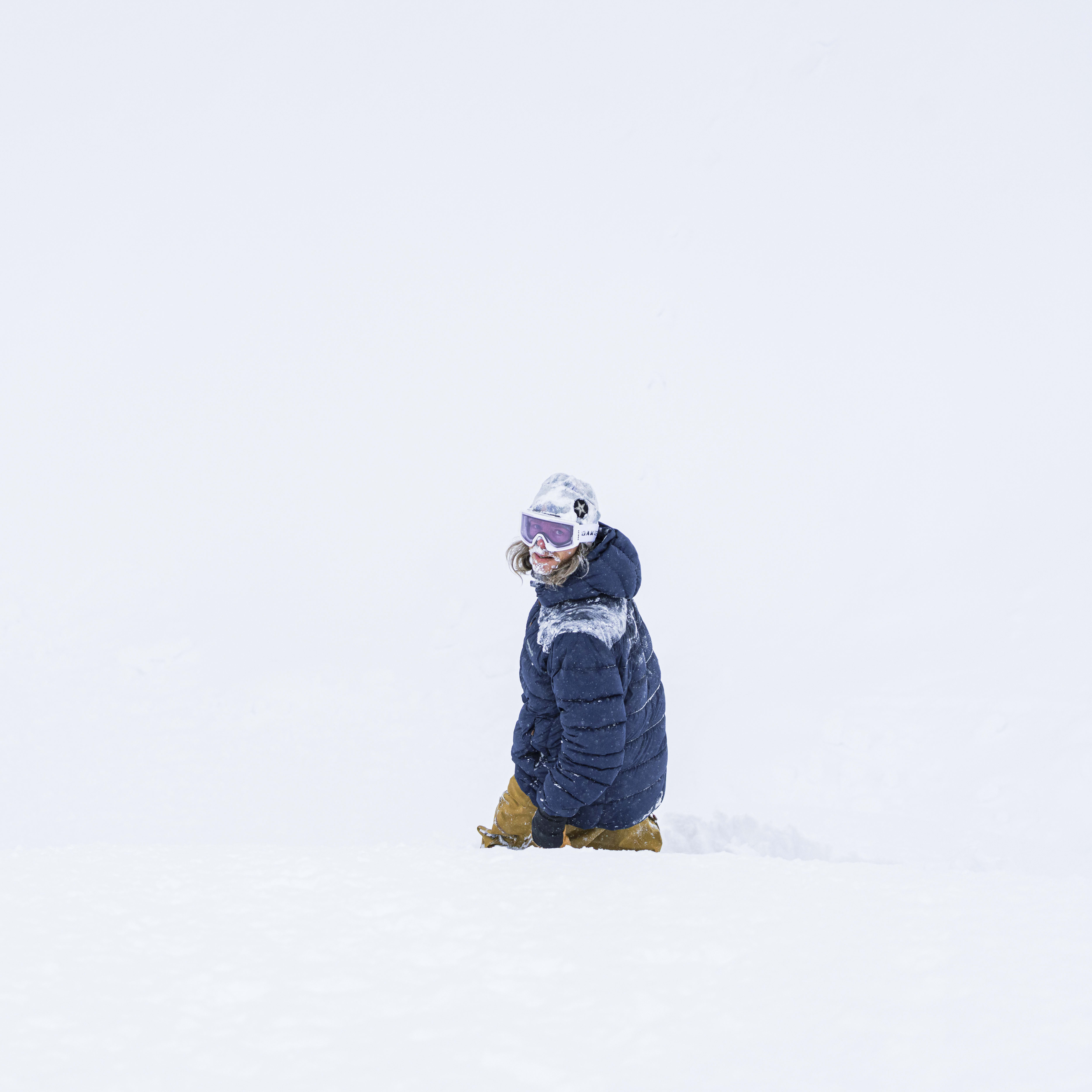 A person wearing a blue Norrøna jacket and goggles sits in the snow.