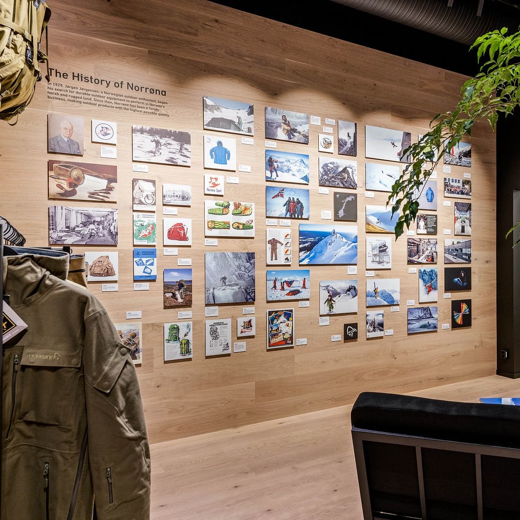 A green Norrøna jacket hangs next to an exhibition wall detailing the history of Norrøna, beside an indoor tree.