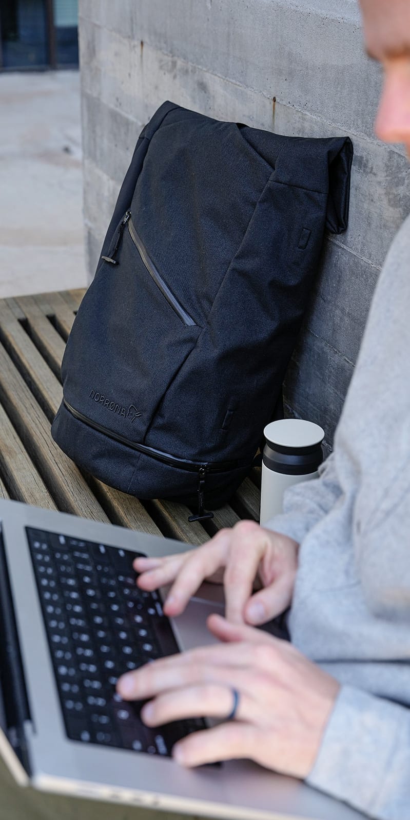 Person in grey Norrøna shirt typing on a laptop next to a black Norrøna backpack.