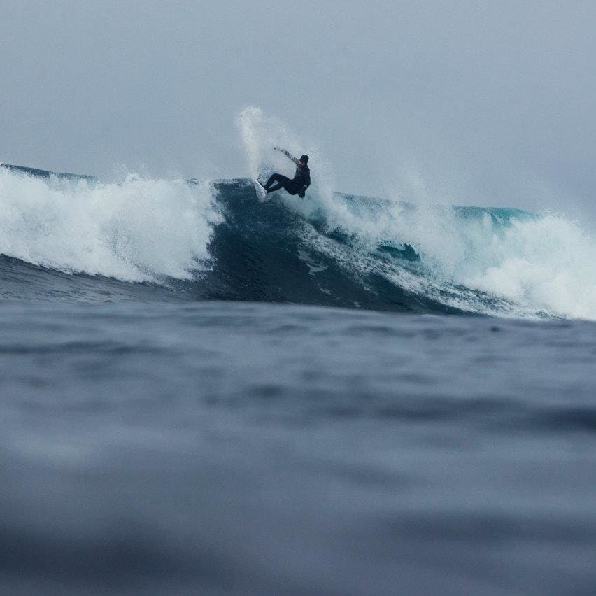 A surfer wearing a Norrøna wetsuit rides a large wave.