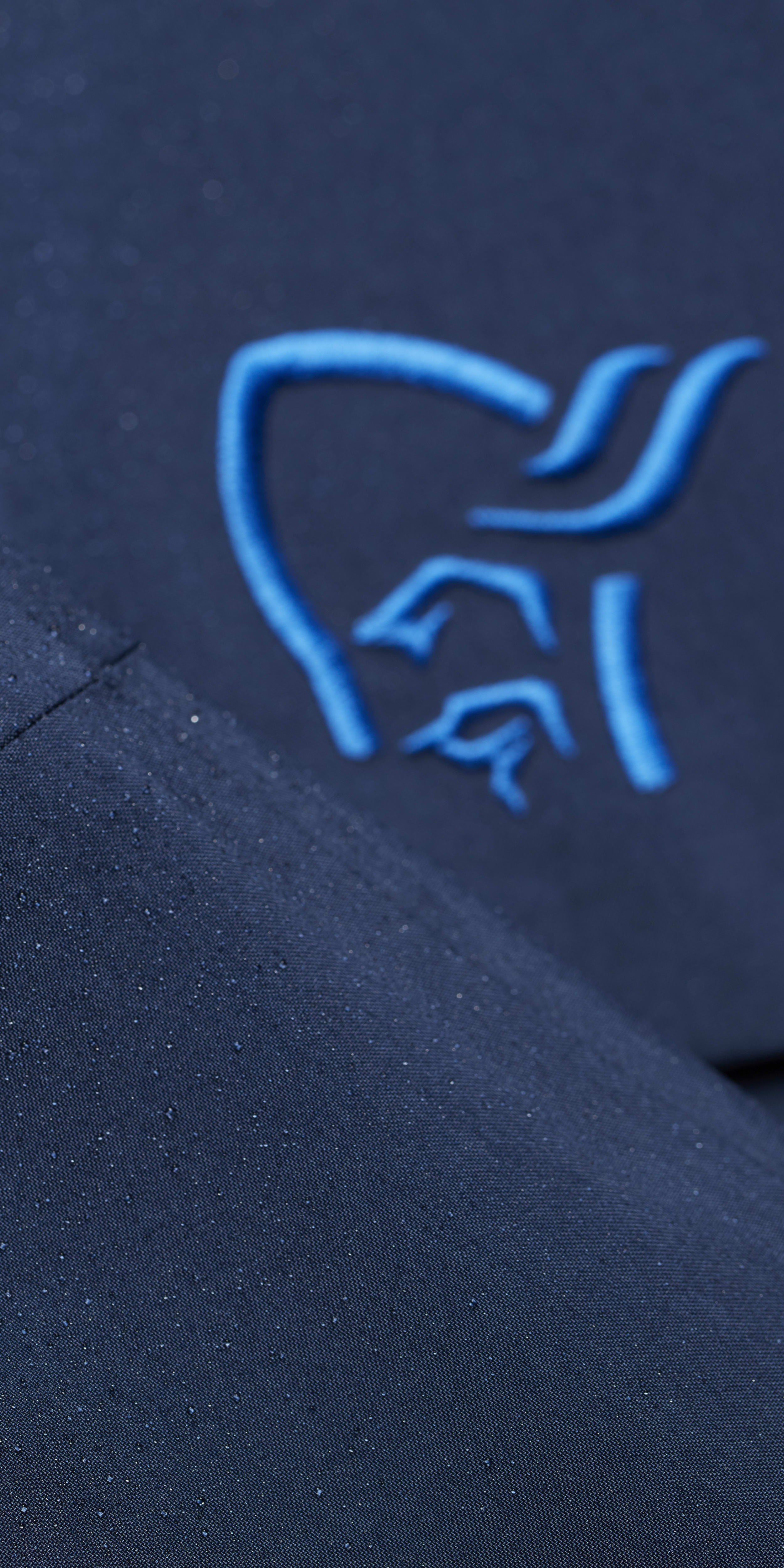 Closeup of a dark blue Norrøna jacket with water droplets on the surface. The zipper is pulled up. 
