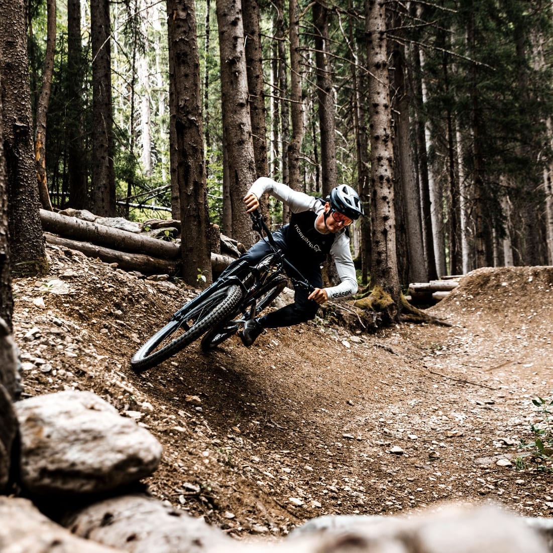 A mountain biker wearing Norrøna apparel leans into a turn on a forest trail.