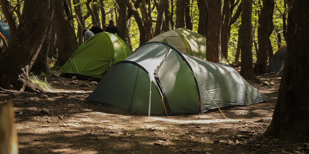 A green Norrøna tent pitched in a forest clearing, surrounded by trees.