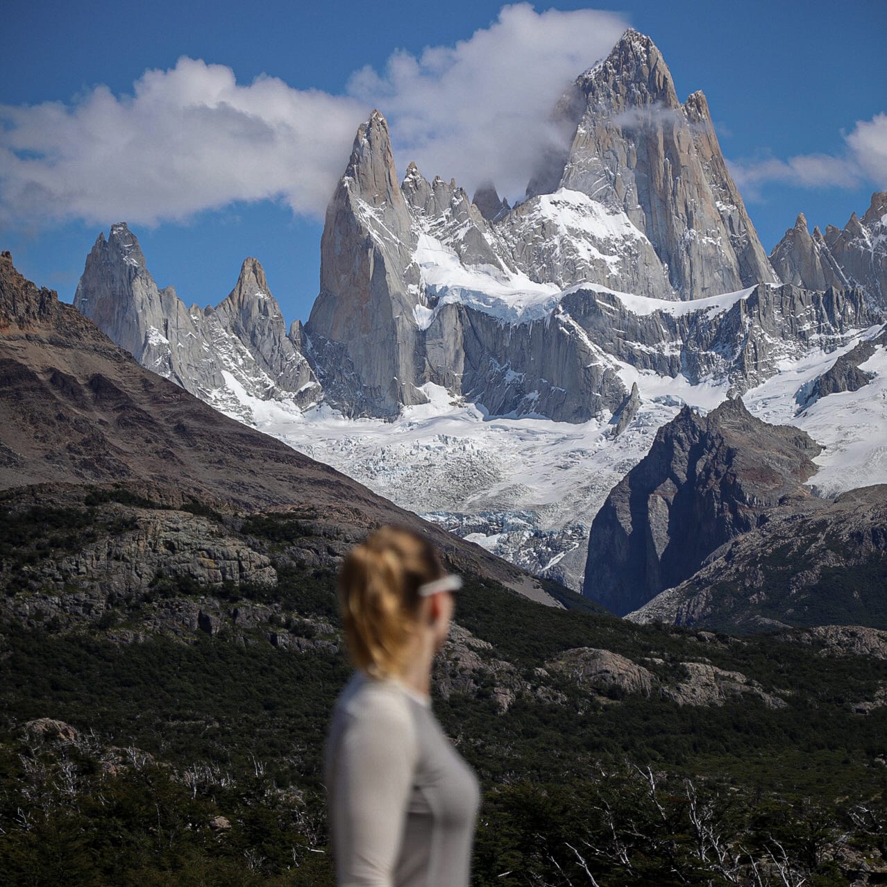 A woman wearing a Norrøna shirt looks towards the snow-capped peaks of the mountain range. 
