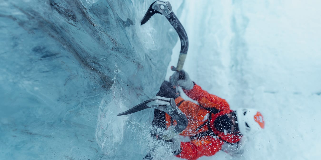 A person ice climbing with an ice axe, wearing a Norrøna jacket and helmet.  
