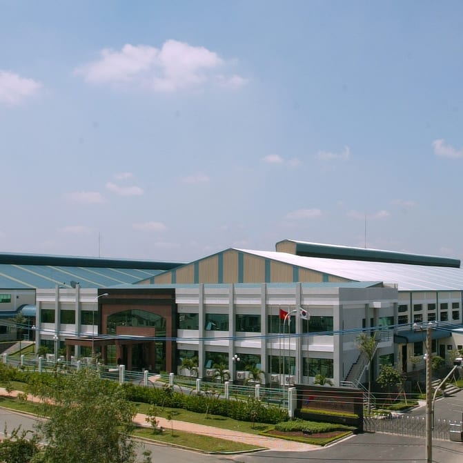 View of a large manufacturing building complex under a bright, slightly cloudy sky.