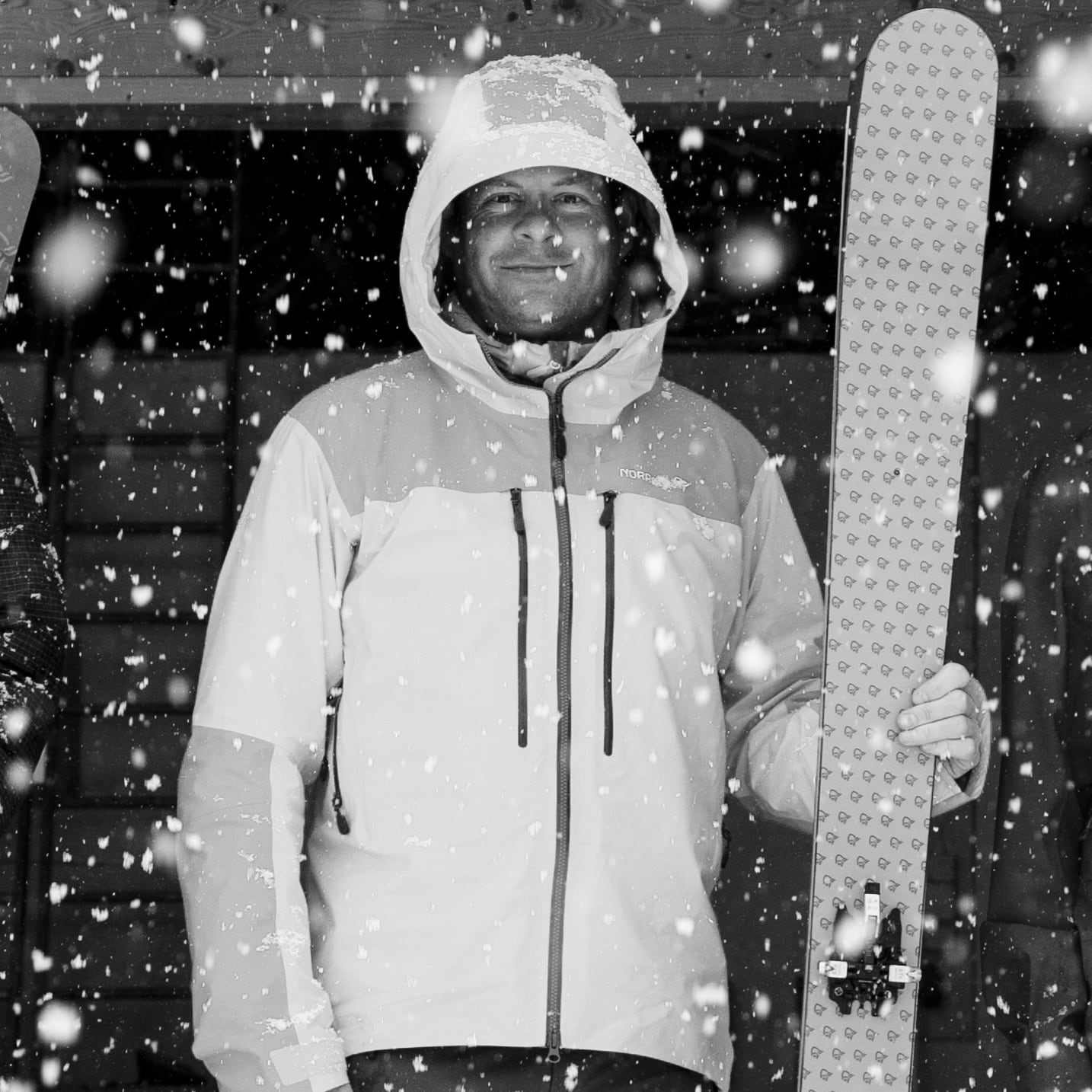 A man in a Norrøna jacket stands in the snow, holding a ski. 
