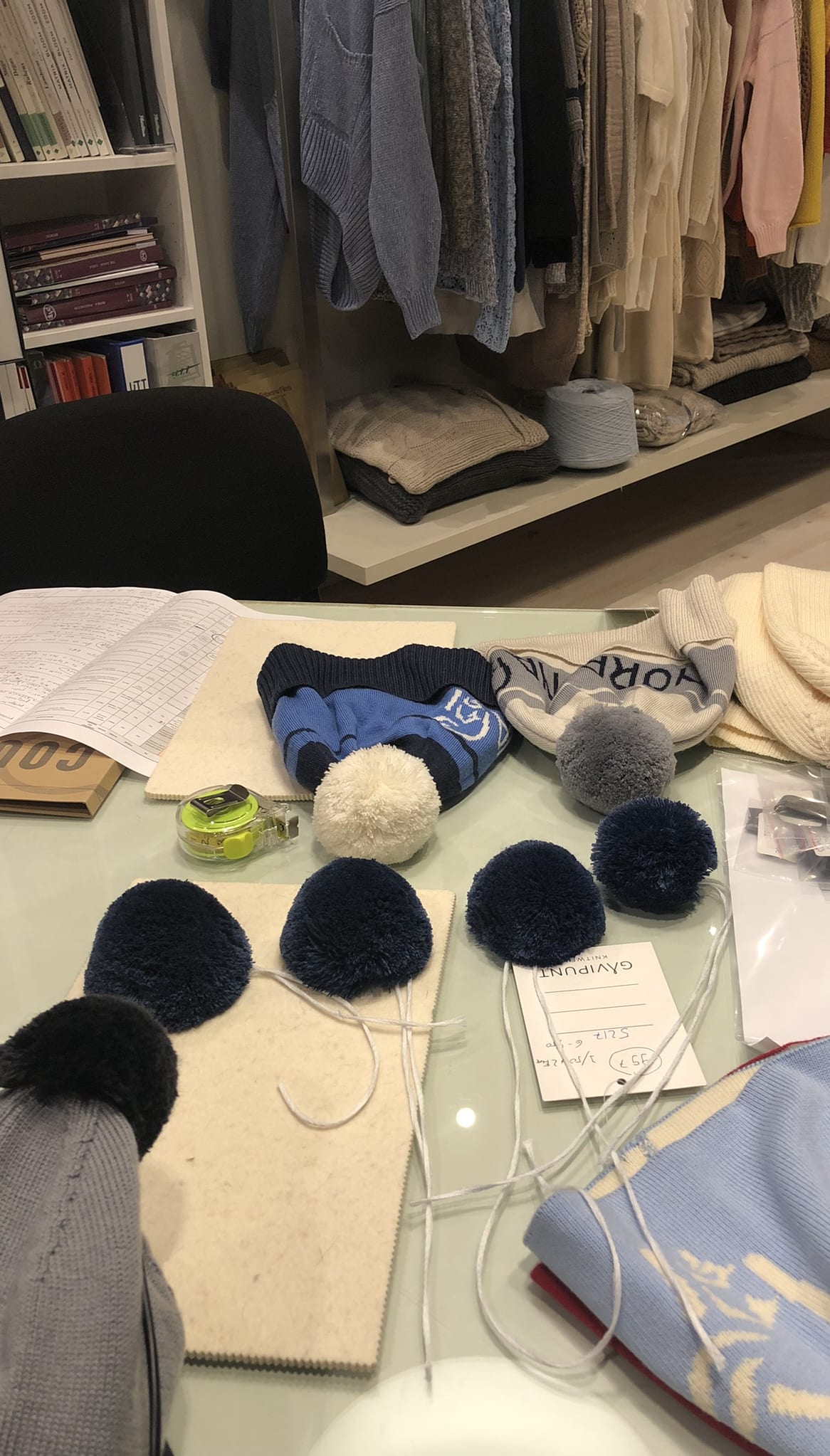 A table with various knitted hats, pom-poms, and other materials, including a tape measure and a tag that reads "GAVIPUNT KNITWEAR 52176-500".