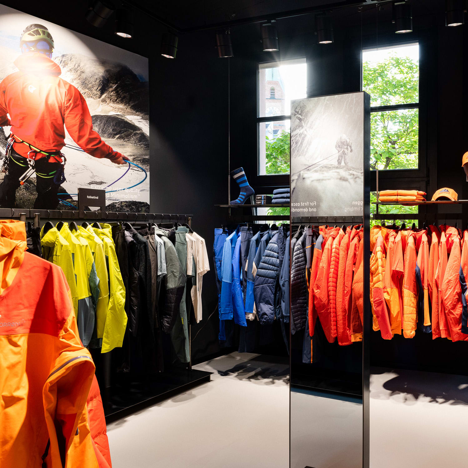A rack of colorful Norrøna jackets in a store. The jackets are hanging on hangers and are arranged in a row.  A mirror is to the left.