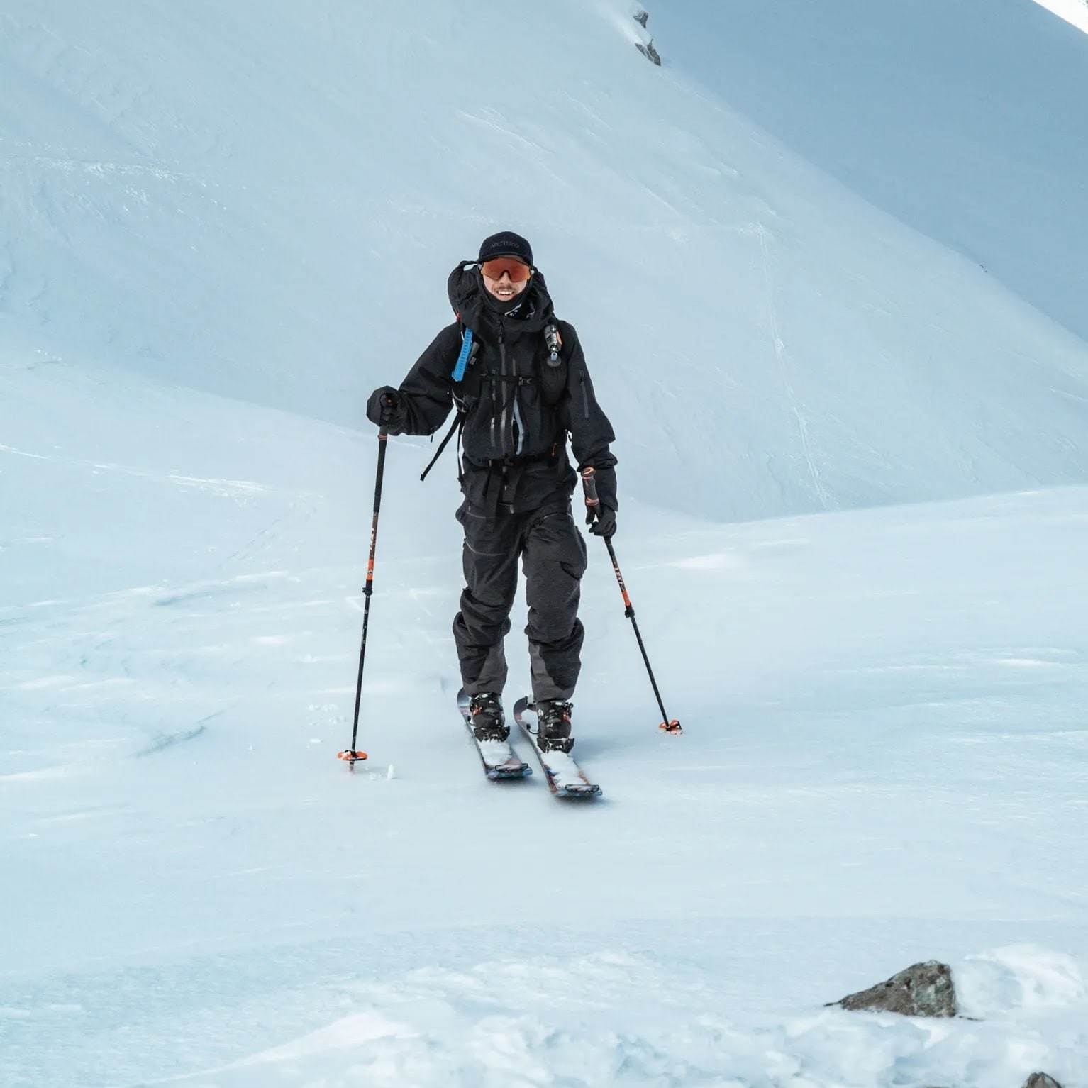 Skier in black Norrøna gear smiles on a snowy mountain slope.