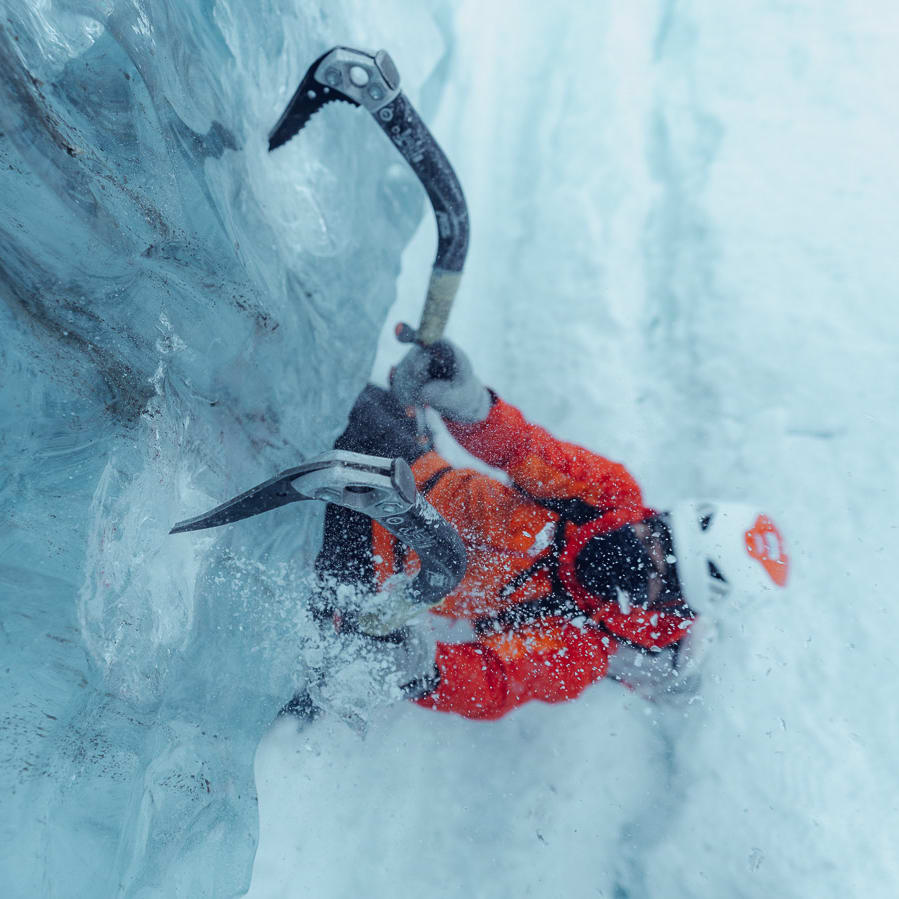 A person ice climbing with an ice axe, wearing a Norrøna jacket and helmet.