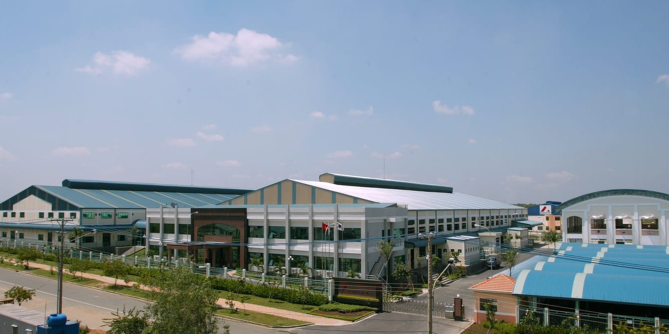 View of a large manufacturing building complex under a bright, slightly cloudy sky.