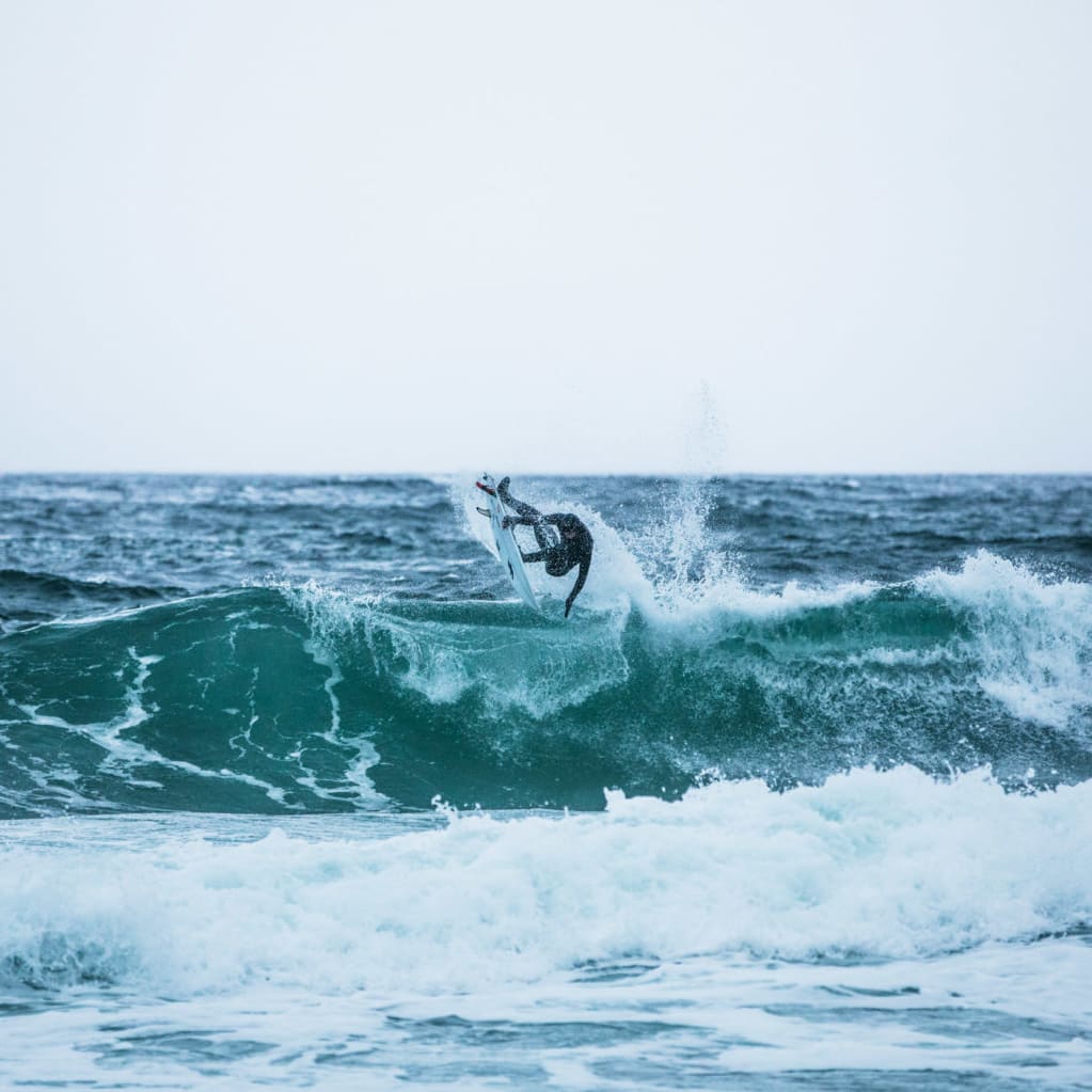 A surfer in a Norrøna wetsuit performs an aerial maneuver on a large wave.