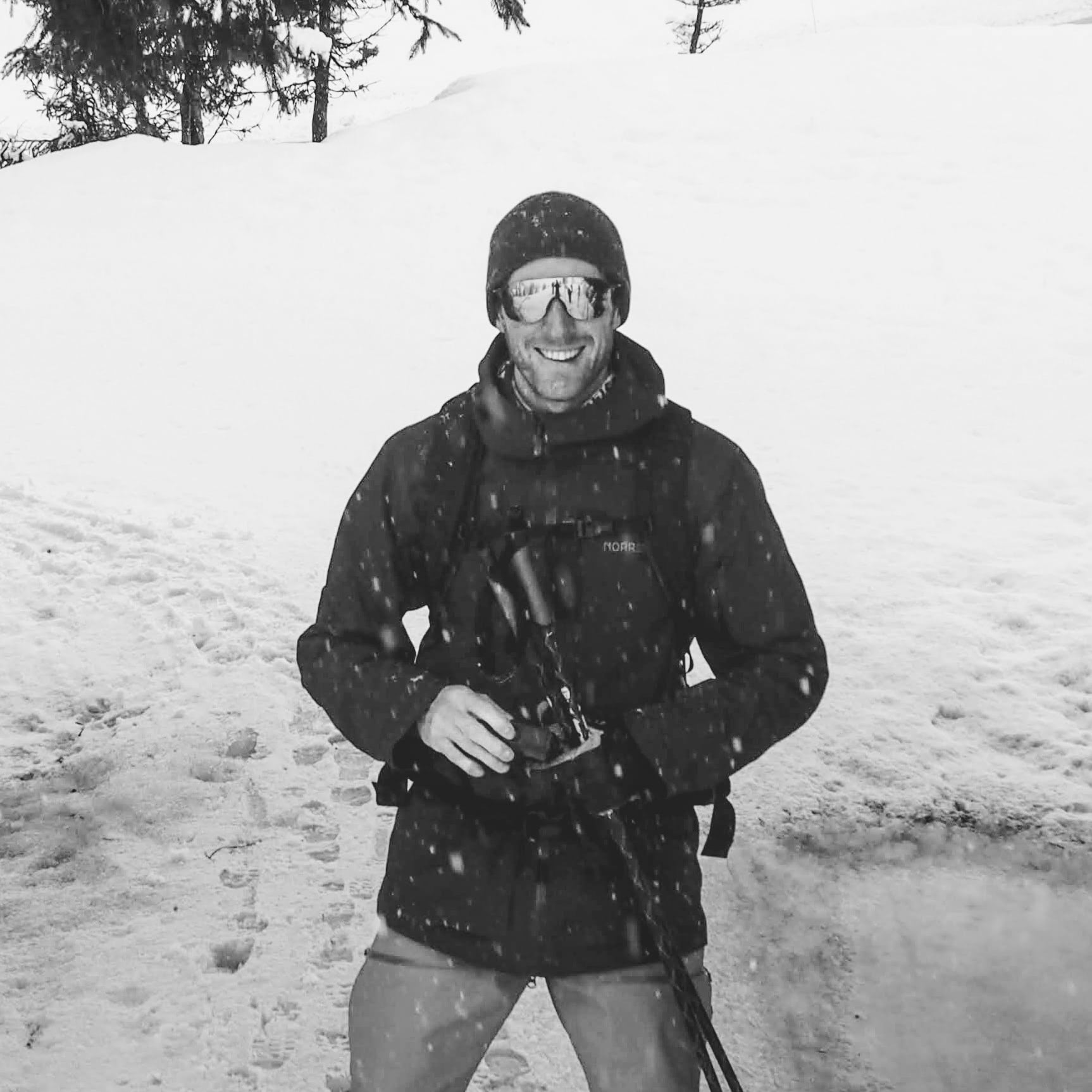 A man wearing a Norrøna jacket and ski goggles smiles in a snowy landscape.
