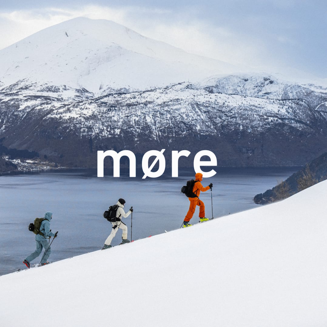 Three skiers in Norrøna outerwear ascend a snowy slope above a fjord. Text overlay: "møre".