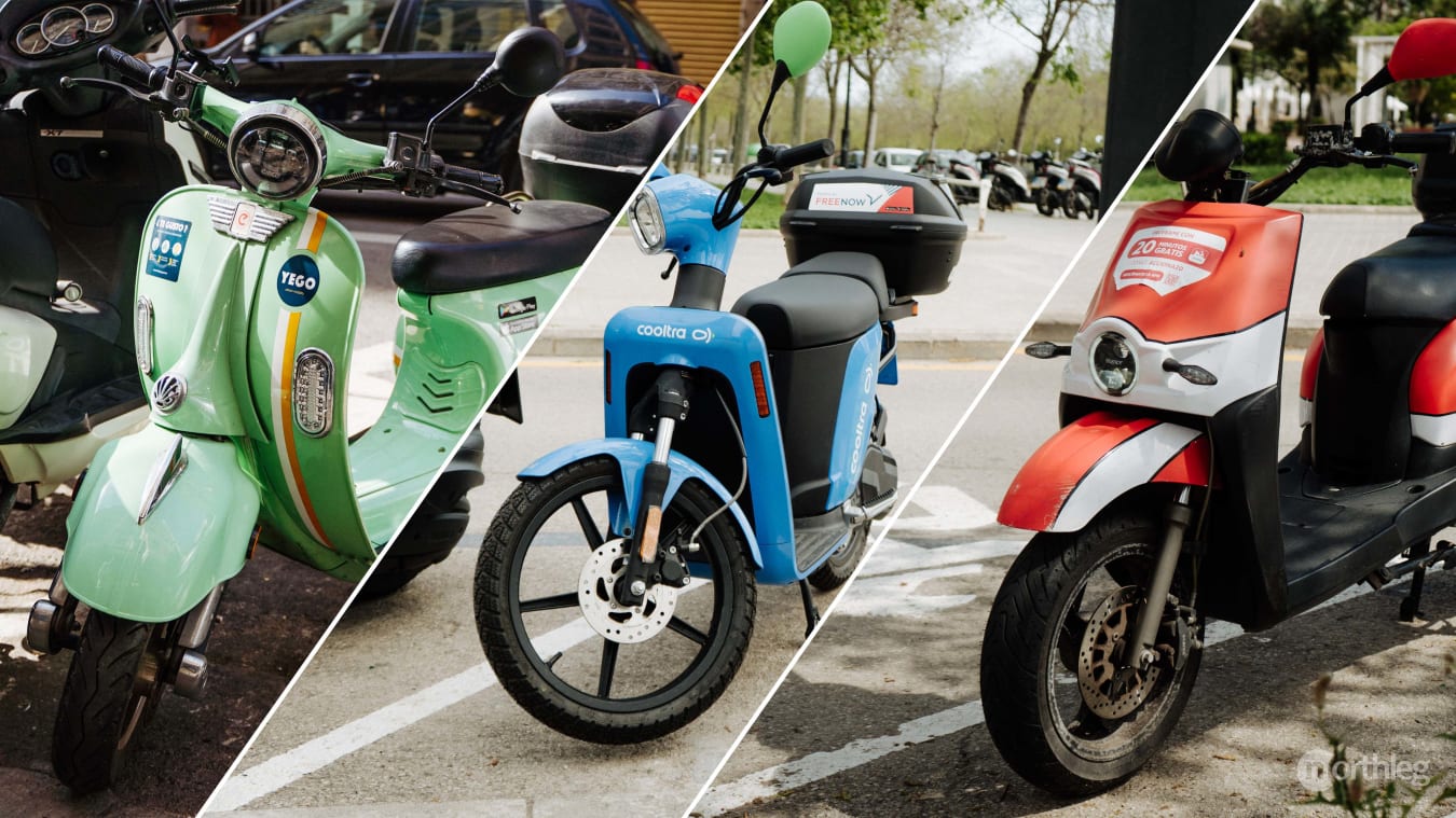 Three electric scooters in different colors (green, blue, and red/white) parked in designated urban parking spaces, representing shared mobility services.