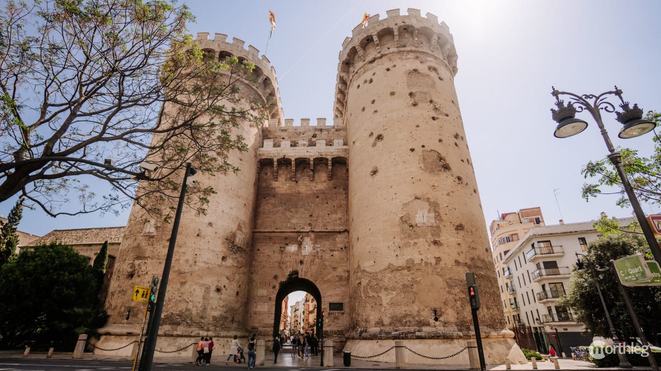 Medieval stone towers with crenellated tops and visible cannon ball marks, forming part of Valencia's historic city gate