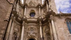 Exterior view of Valencia Cathedral featuring elaborate Baroque facade with white stone columns, ornate sculptures, and a circular window.