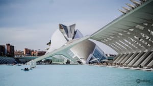 Futuristic white architectural complex with curved buildings and geometric shapes, situated beside a blue reflecting pool in Valencia, Spain.