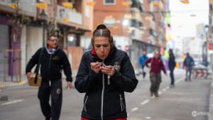 A person in a black jacket holding a small firecracker on a street during Valencia's Las Fallas festival.
