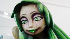 A vibrant green and purple cartoon-like sculpture of a figure with large expressive eyes, representing a traditional Fallas festival ninot.