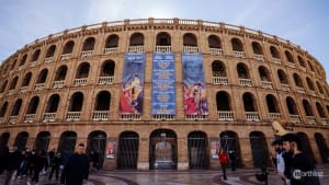 Large circular brick bullring with multiple arched levels, adorned with bullfighting event posters, located in Valencia, Spain.