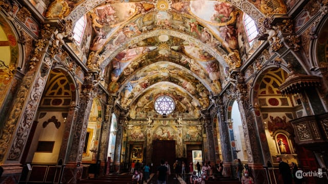 Interior view of the Church of Saint Nicholas, featuring elaborately painted vaulted ceilings, golden ornamentations, and arched windows filled with religious artwork.