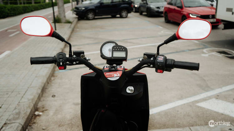 Close-up of an Acciona electric scooter's instrument panel with red-trimmed side mirrors, showing dashboard and charging ports.