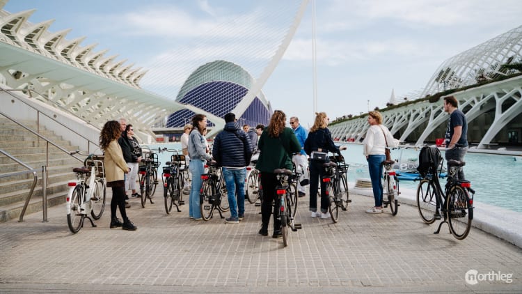 Cyclists riding bikes near the white, curved architectural structures of Valencia's City of Arts and Sciences complex.