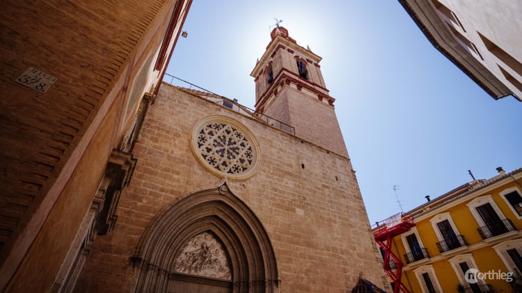 Gothic church exterior with ornate rose window and bell tower, set against blue sky in Valencia's old town.