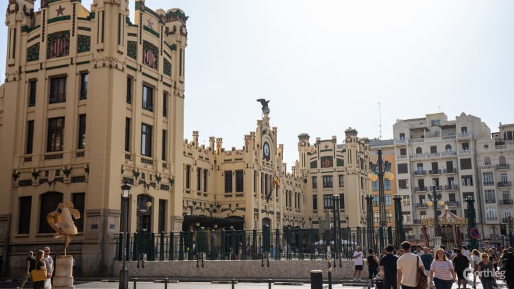 Exterior view of Valencia's North Station, a Modernist-style building with cream-colored walls, decorative elements, and a central clock tower with an eagle statue.