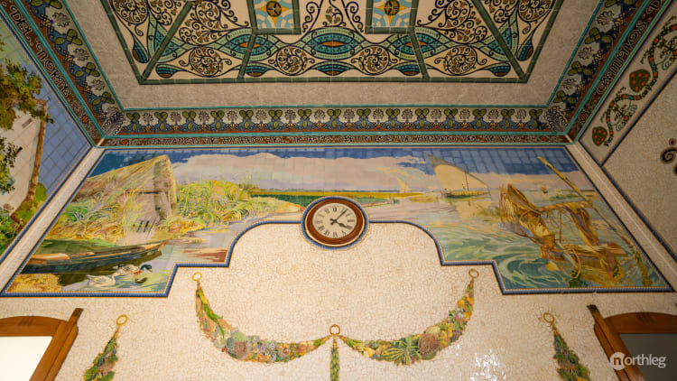 Ornate interior of Valencia's North Station with colorful mosaic tiles, decorative ceiling, landscape mural, and central clock.