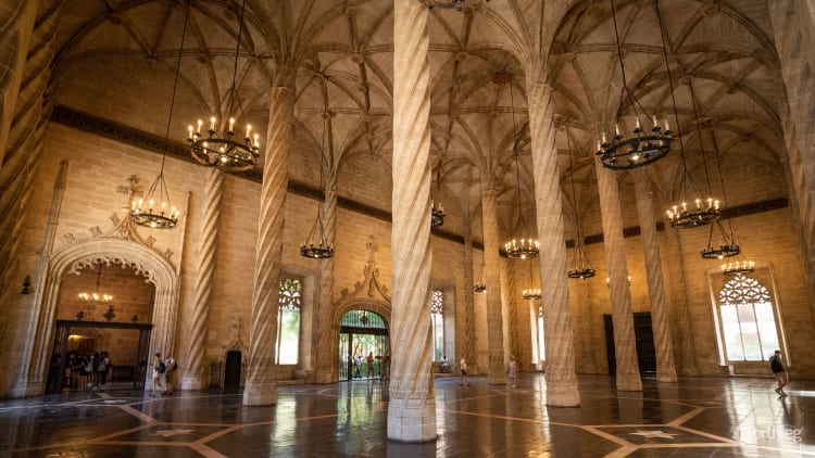 Interior of La Lonja de la Seda with tall twisted stone columns, vaulted Gothic ceiling, and hanging wrought iron chandeliers creating a majestic medieval trading hall atmosphere.