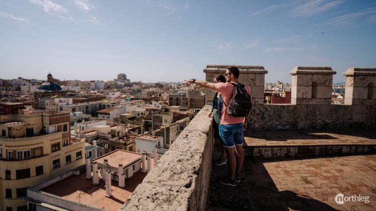 Travelers overlooking Valencia's rooftops from the historic stone walls of Torres de Quart on a sunny day.