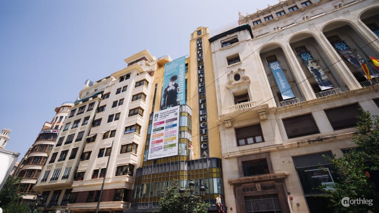 Historic buildings with architectural variety including the Rialto Theater and Filmoteca, with cinema posters and banners displayed on sunny day in Valencia.