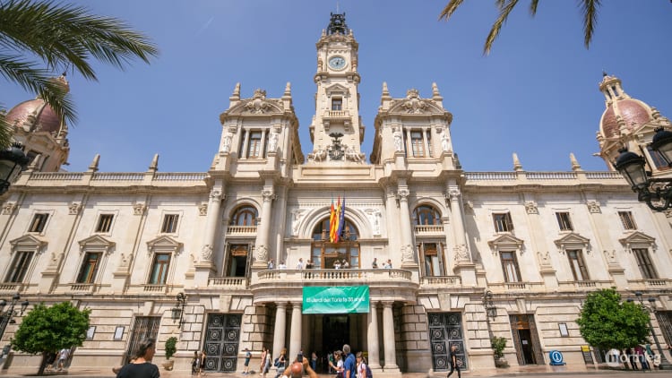 Majestic white stone Town Hall building in Valencia with clock tower, decorative architectural elements, and people walking in the foreground.