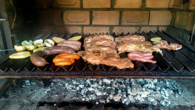 Variety of meats and vegetables grilling on a brick barbecue with hot coals underneath.