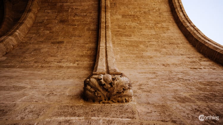 Close-up of ornate stone architectural element with leaf-like carving at the base of curved stone walls in warm golden tones.