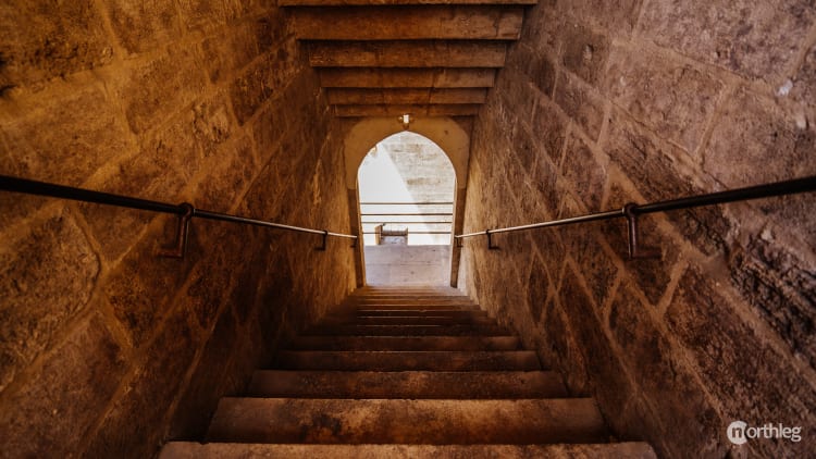 Interior stone staircase with arched doorway, showing steep steps inside Torres de Serranos with metal handrails.