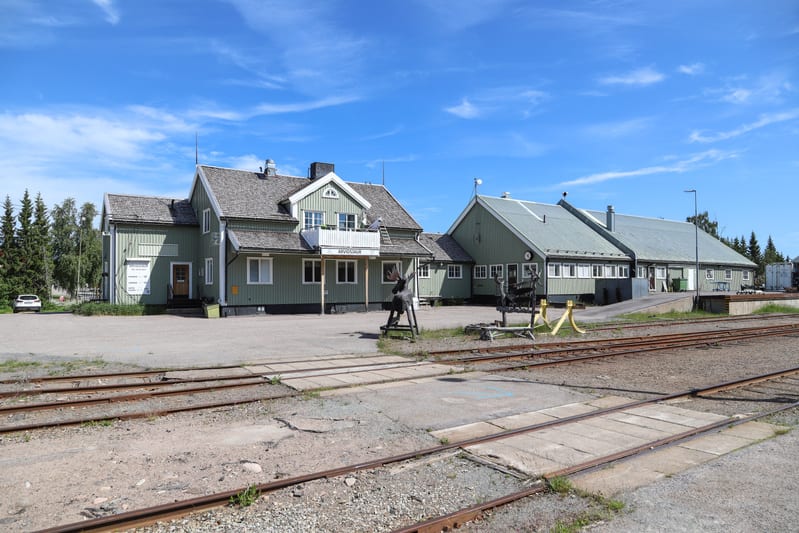Bilden visar ett grönfärgat hus med träfasad och ett grått tak. Entrén är markerad med en dörr och flera fönster. Till höger om huset finns en utökning av byggnaden, också den grönmålad med flera fönster och ett metalltak. Framför byggnaderna ligger