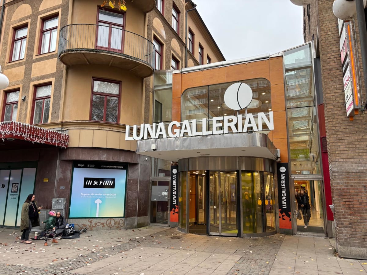 Bilden visar entréområdet till "Luna Gallerian", med dess skyltning tydligt synlig över den roterande dörren. Till vänster om entrén finns en skyltfönster med reklam för "IN & FINN" och texten "Öppnar här under våren 2026". Längre till vänster syns d