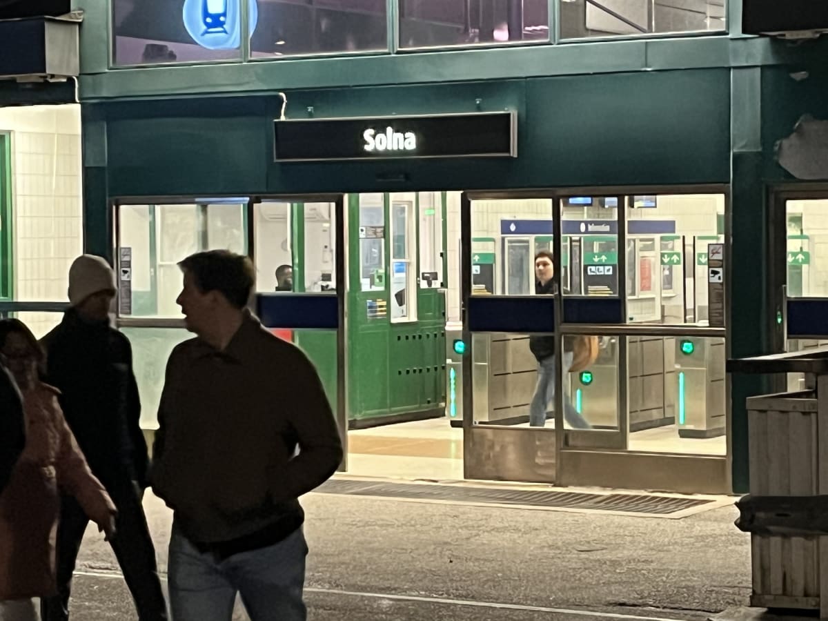 Bilden visar entréområdet till tunnelbanestationen Solna. En skylt med texten "Solna" är placerad ovanför ingången. Ovanför skylten, i fönstret, syns en blå symbol som föreställer en tunnelbanevagn. Entrén består av automatiserade spärrar och biljett