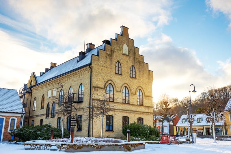 En bild visar en gul tegelbyggnad med detaljerad arktitektur och spetsbågade fönster. Byggnaden har ett brant tak med snö på, samt gavlar i trappstegsform. Två svarta spiraltrappor, troligen nödutgångar, är fästa på byggnadens utsida. Framför byggnad